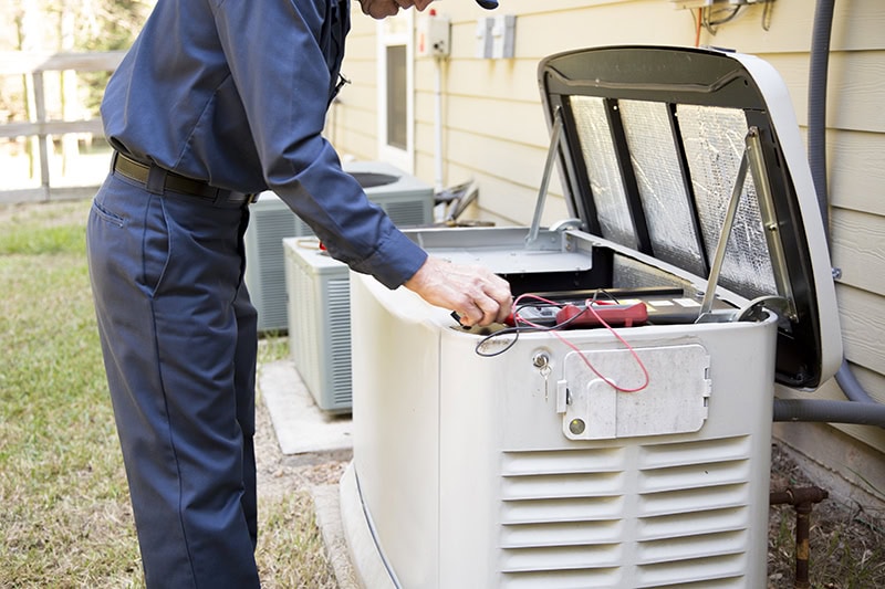 Maintaining Your Whole-Home Generator for Reliable Performance. Photo of a technician performing maintenance on a generator installed outside of a home.
